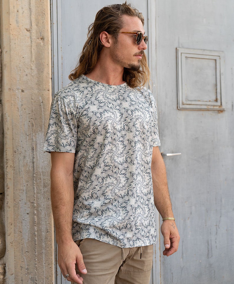 May include: A white t-shirt with a black and white patterned design. The shirt has a crew neck and short sleeves.