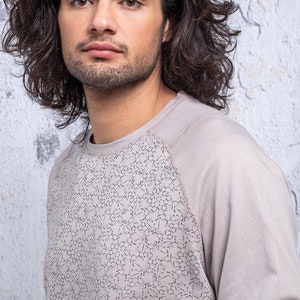May include: A light gray long-sleeved shirt with a geometric pattern on the front. The shirt has a raglan sleeve design.