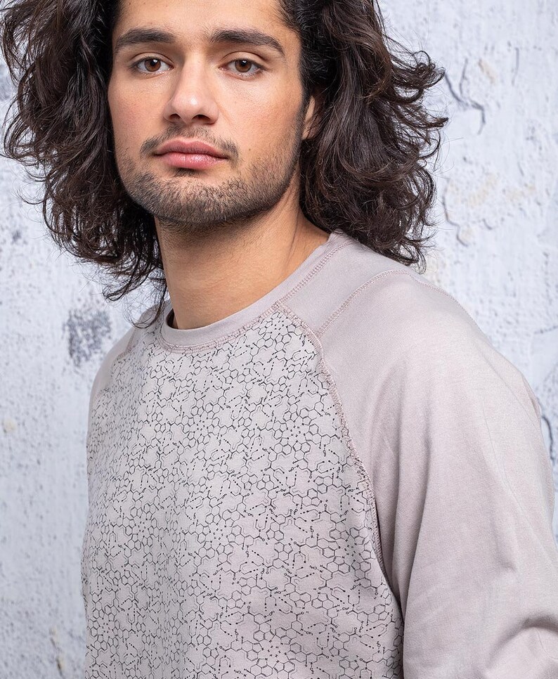 May include: A light gray long-sleeved shirt with a geometric pattern on the front. The shirt has a raglan sleeve design.
