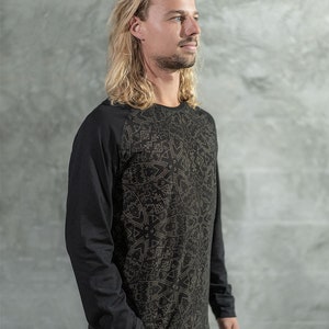 May include: A black long-sleeve shirt with a geometric pattern in gold. The shirt has a crew neck and raglan sleeves.