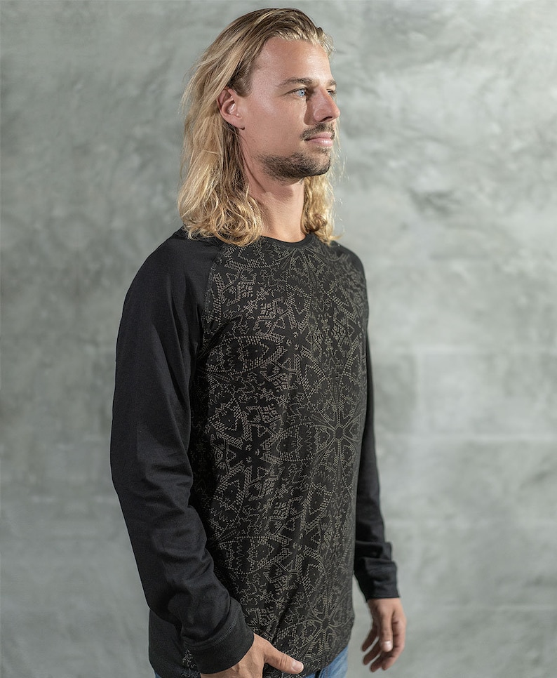 May include: A black long-sleeve shirt with a geometric pattern in gold. The shirt has a crew neck and raglan sleeves.