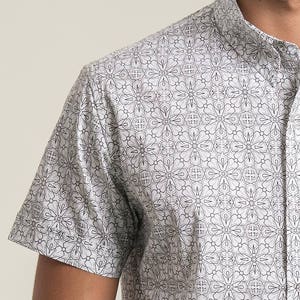Pode incluir: Uma camisa branca de manga curta com um padr&atilde;o geom&eacute;trico preto.