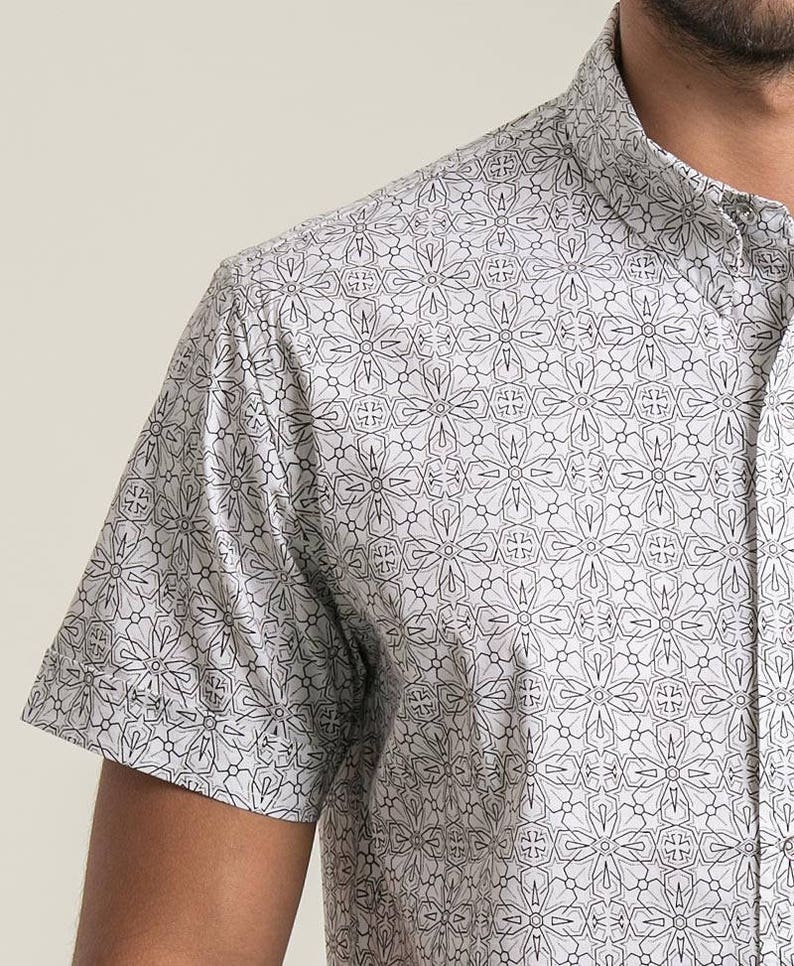 Pode incluir: Uma camisa branca de manga curta com um padr&atilde;o geom&eacute;trico preto.