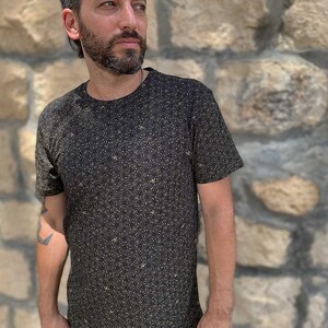 Puede incluir: Una camiseta negra de manga corta con un patr&oacute;n geom&eacute;trico dorado.