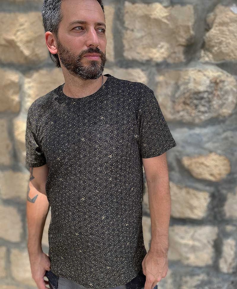 Puede incluir: Una camiseta negra de manga corta con un patr&oacute;n geom&eacute;trico dorado.