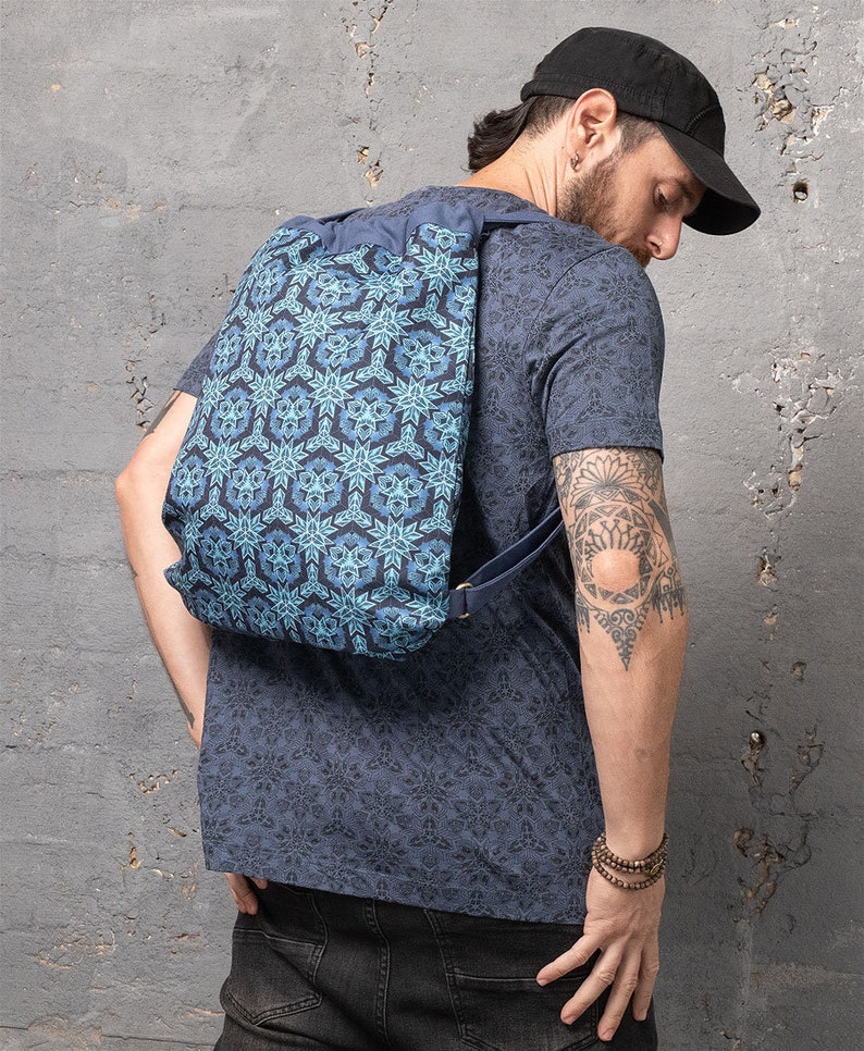 Puede incluir: Una mochila azul de cord&oacute;n con un patr&oacute;n geom&eacute;trico. La mochila la lleva puesta una persona con un tatuaje en el brazo.
