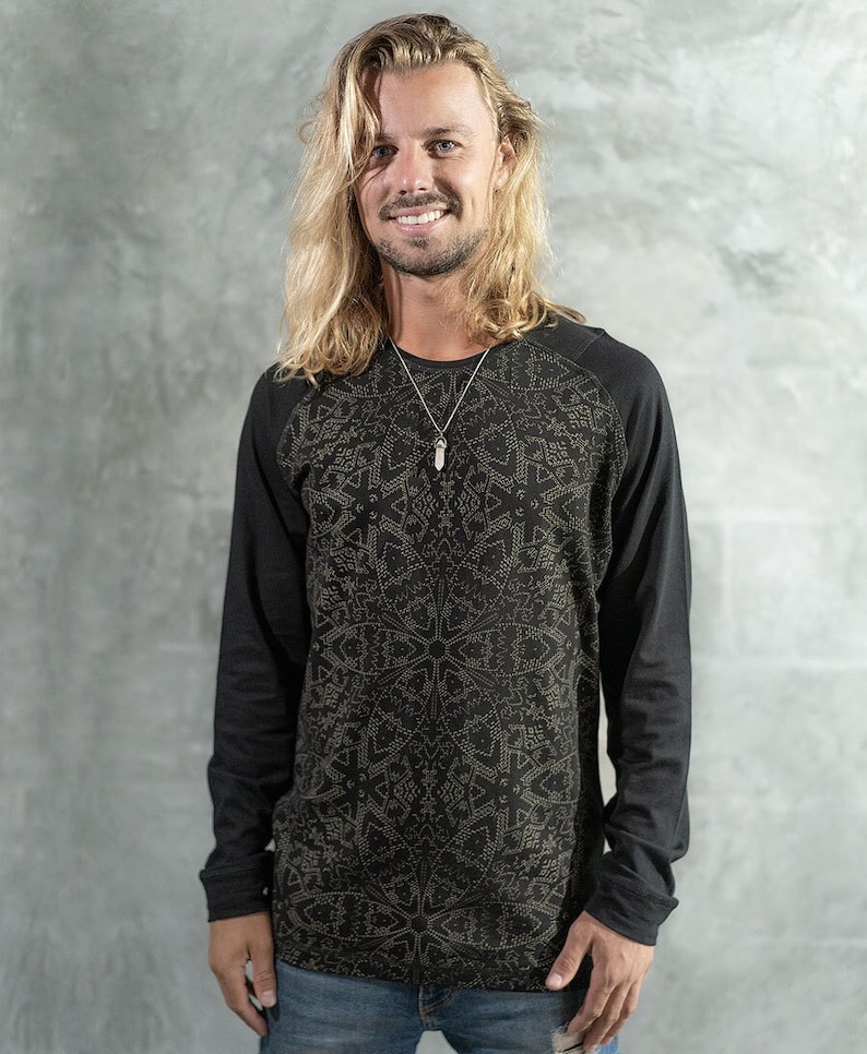 May include: A black long-sleeved shirt with a geometric pattern in gold. The shirt has a raglan sleeve design.