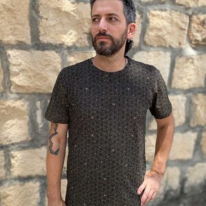 Puede incluir: Una camiseta negra con un peque&ntilde;o patr&oacute;n intrincado de puntos dorados. La camiseta tiene cuello redondo y mangas cortas.
