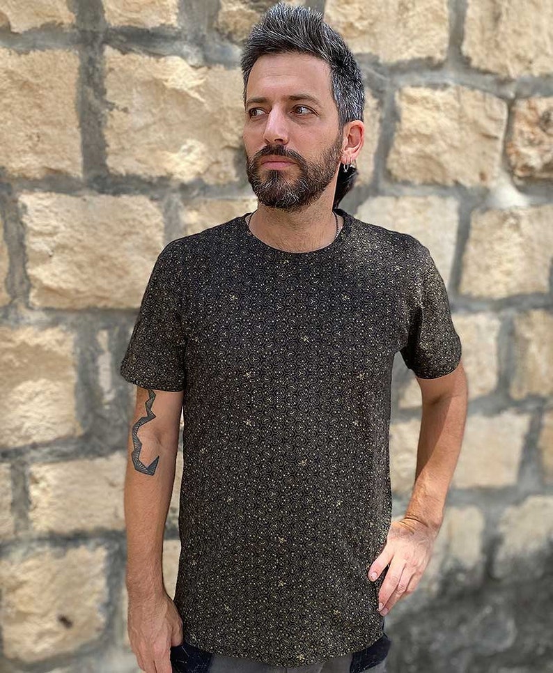 Puede incluir: Una camiseta negra con un peque&ntilde;o patr&oacute;n intrincado de puntos dorados. La camiseta tiene cuello redondo y mangas cortas.