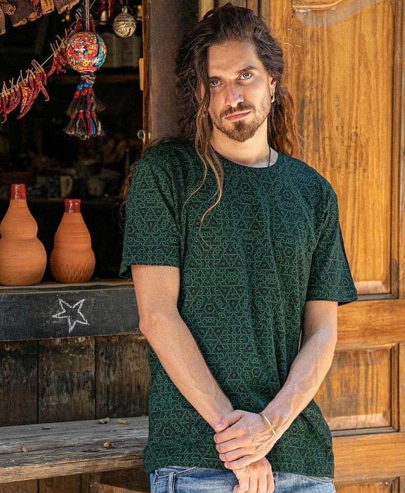 May include: A man with long brown hair is wearing a green t-shirt with a geometric pattern. The shirt has a crew neck and short sleeves.