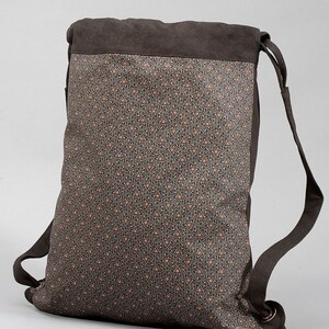 May include: A brown backpack with a geometric pattern. The top and straps are a solid brown, while the main body features a repeating pattern of small triangles in shades of brown and orange. The bag has adjustable straps.