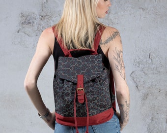 May include: A dark blue and red backpack with a geometric pattern. The backpack has a flap with a buckle closure and a drawstring closure at the bottom.
