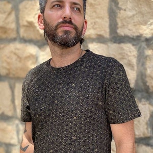 Puede incluir: Una camiseta negra con un patr&oacute;n geom&eacute;trico dorado.