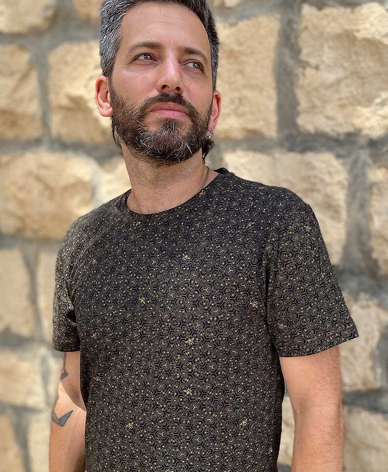 Puede incluir: Una camiseta negra con un patr&oacute;n geom&eacute;trico dorado.