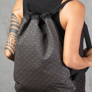 May include: A black drawstring backpack with a geometric pattern in shades of brown and orange. The bag has black straps and a black drawstring closure. The backpack is worn over the shoulders.