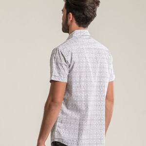 Pode incluir: Uma camisa branca de manga curta com bot&otilde;es e um padr&atilde;o geom&eacute;trico preto e branco.