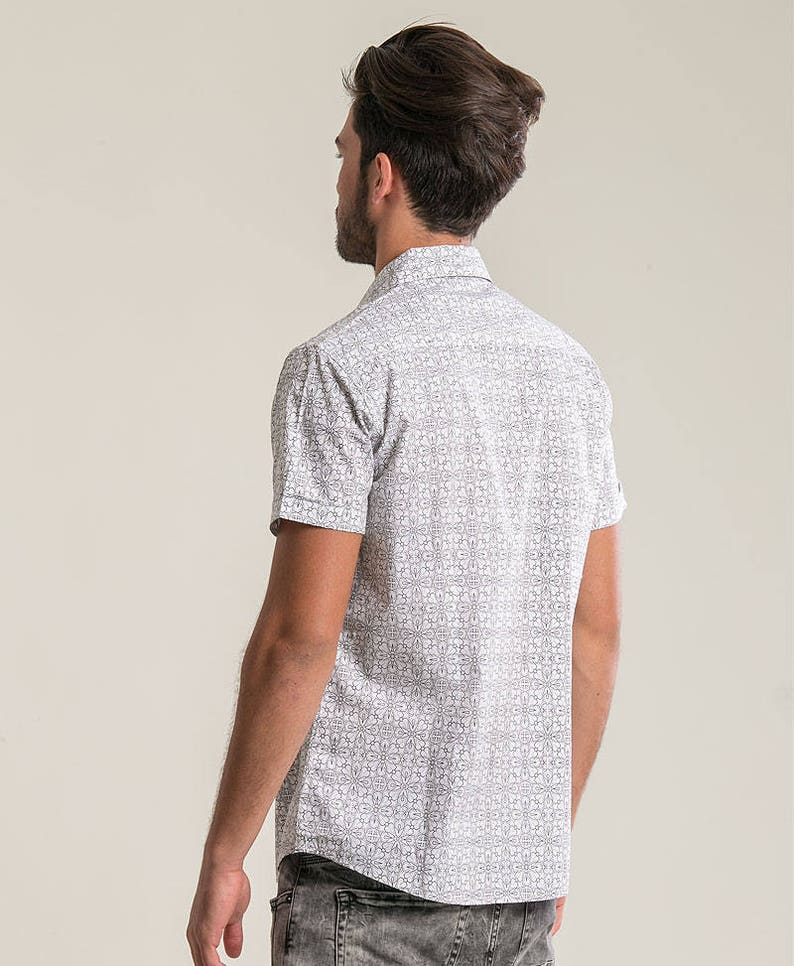 Pode incluir: Uma camisa branca de manga curta com bot&otilde;es e um padr&atilde;o geom&eacute;trico preto e branco.