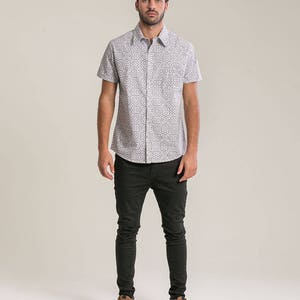 May include: A white short-sleeved button-down shirt with a geometric pattern. The shirt is paired with black skinny jeans and brown leather boots.