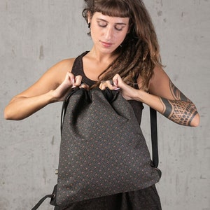 May include: A dark gray drawstring backpack with a repeating pattern of small orange shapes. The backpack has black straps and a drawstring closure. The bag is made of a textured fabric.