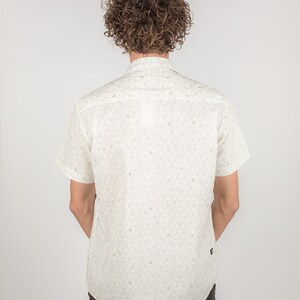 May include: A white short-sleeved button-down shirt with a small, all-over print of green leaves. The shirt has a collar and a pocket on the left side.