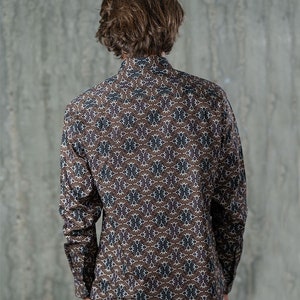 May include: A long-sleeved button-down shirt with a brown, white, and purple geometric pattern. The shirt is made of a lightweight fabric and has a classic collar and buttoned cuffs. The shirt is shown from the back.