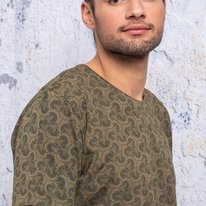 May include: A green short-sleeved t-shirt with a geometric pattern. The pattern is made up of small, repeating shapes that resemble flowers.