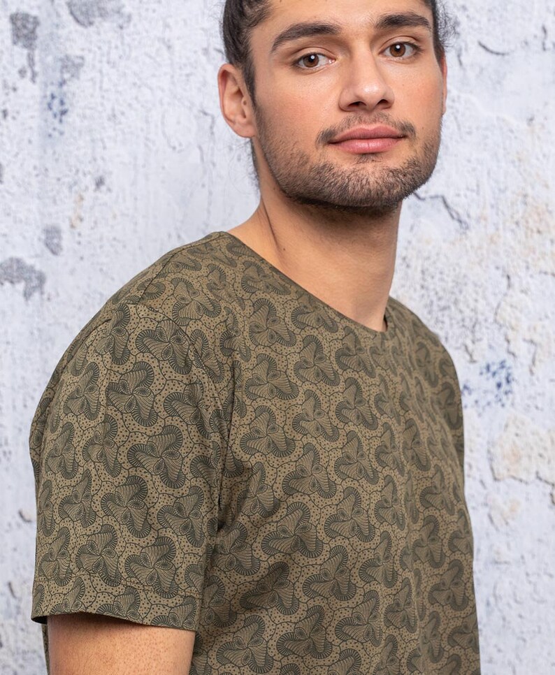 May include: A green short-sleeved t-shirt with a geometric pattern. The pattern is made up of small, repeating shapes that resemble flowers.
