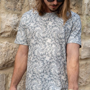 May include: A white t-shirt with a black and gray abstract pattern. The pattern is a repeating design of swirls and circles.