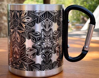 Pode incluir: Uma caneca de viagem de aço inoxidável com um padrão geométrico preto e uma alça de mosquetão preta.