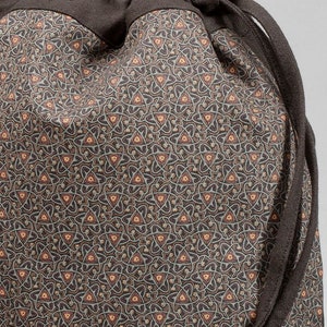 May include: A drawstring bag with a repeating pattern of interconnected shapes and triangles in shades of brown, tan, and gray. The top and drawstring are a solid dark brown color. The bag is made of fabric.