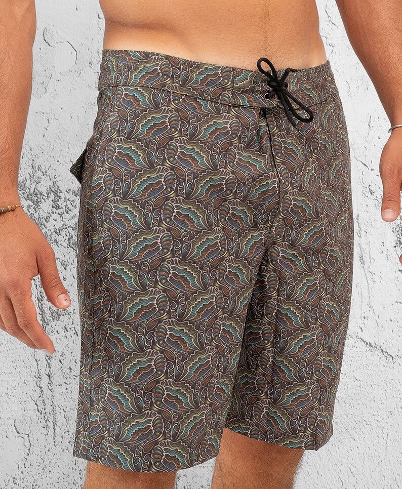 May include: Brown swim trunks with a paisley pattern. The trunks have a drawstring waist and a side pocket.