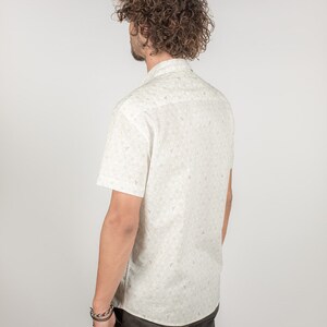 May include: A white short-sleeved button-down shirt with a small, repeating pattern of green leaves. The shirt has a collar and a button-up front.