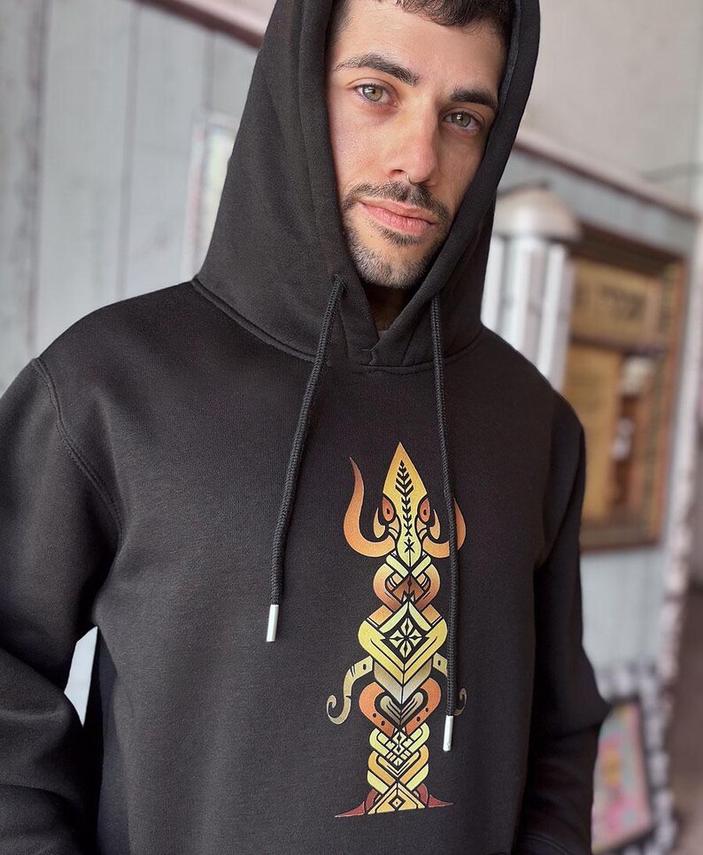 May include: Black hooded sweatshirt with a detailed, colorful graphic on the front. The graphic features a symmetrical design with orange, yellow, and brown elements. The hoodie has a drawstring and a hood.