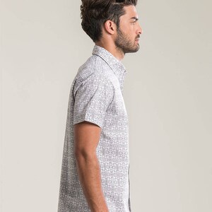 Pode incluir: Uma camisa branca de manga curta com bot&otilde;es e um padr&atilde;o geom&eacute;trico preto e branco.
