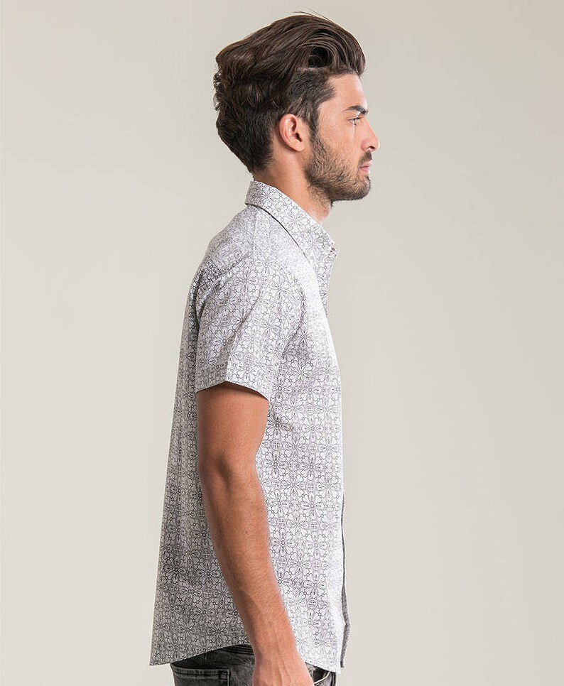 Pode incluir: Uma camisa branca de manga curta com bot&otilde;es e um padr&atilde;o geom&eacute;trico preto e branco.