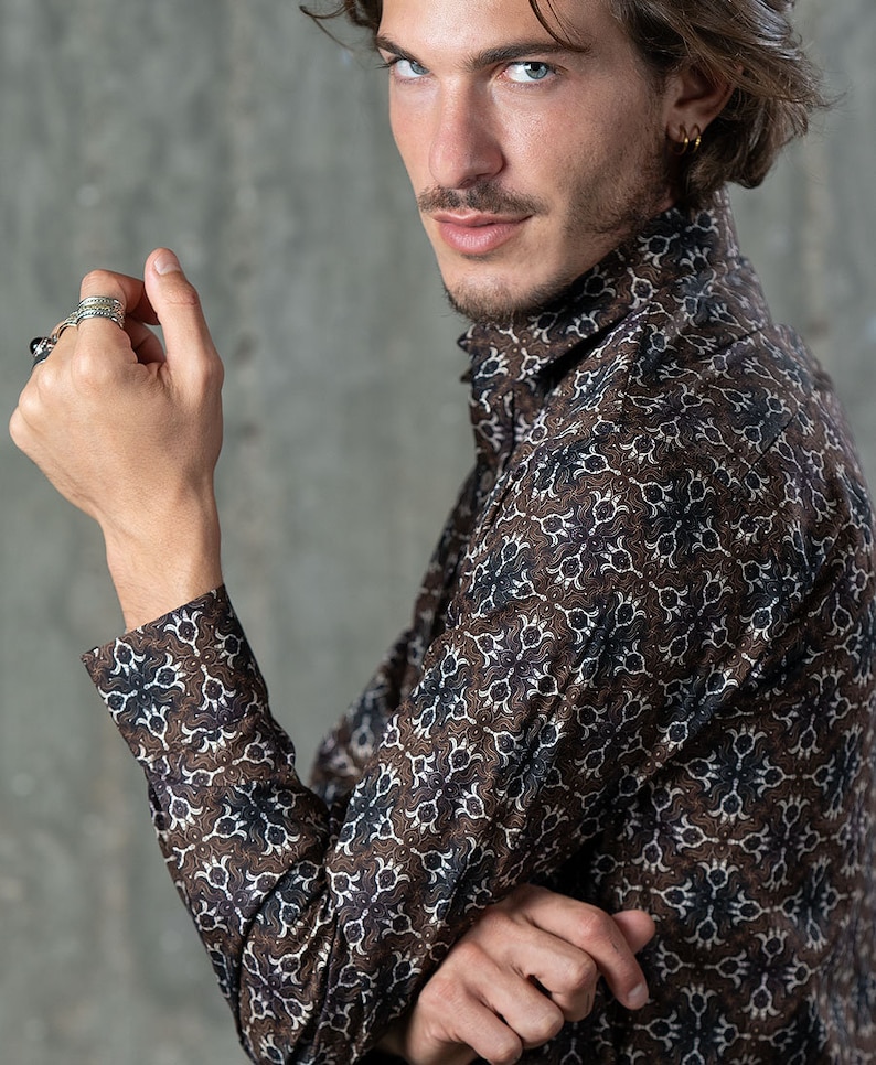 May include: A brown button-up shirt with a repeating white and navy blue floral pattern. The long-sleeved shirt has a high collar and is worn by a person. The shirt is made of a soft, comfortable material.