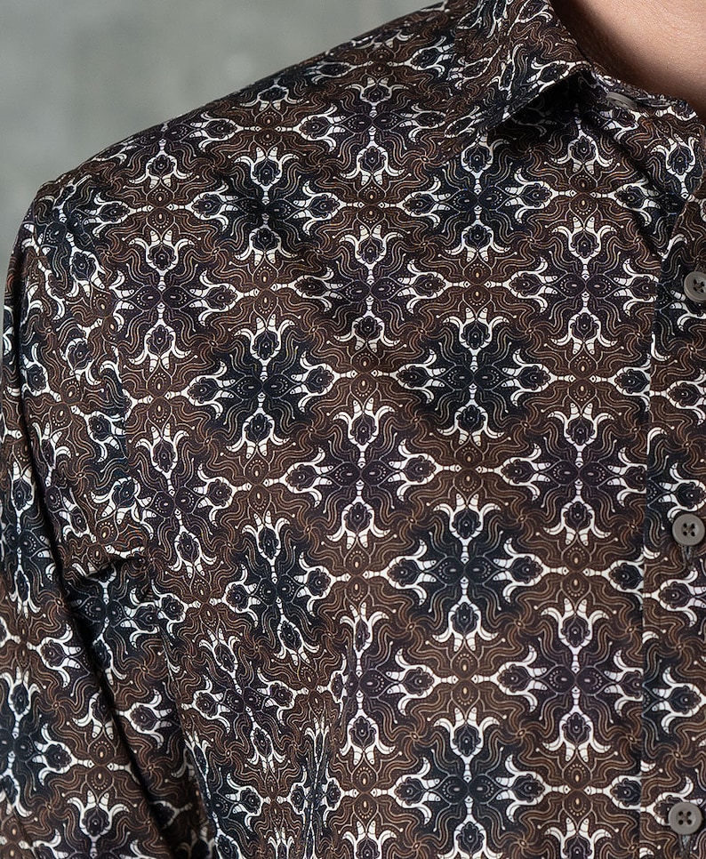 May include: Close-up of a button-down shirt with a repeating geometric pattern in brown, white, and navy blue. The shirt's fabric has a subtle sheen, and the collar and buttons are visible.