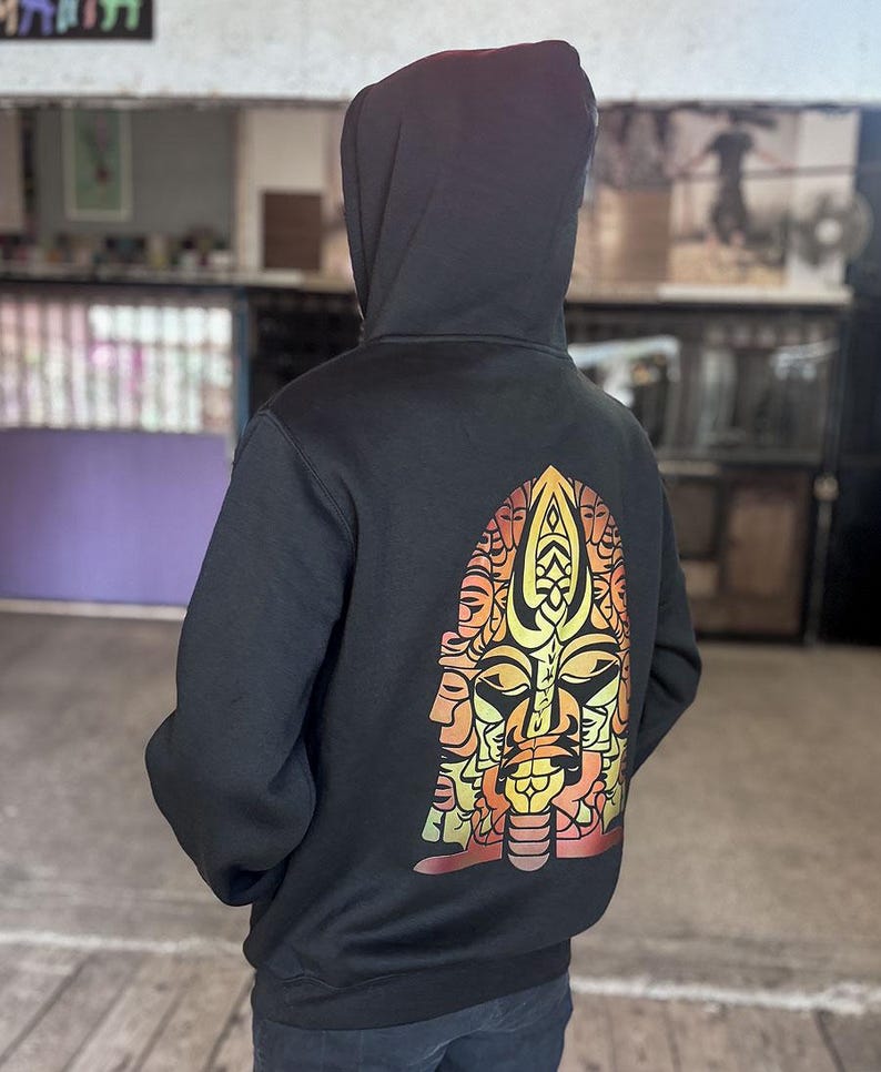 May include: Black hooded sweatshirt with a colorful graphic on the back. The graphic is a stylized face with orange, yellow, and red tones. The sweatshirt has a drawstring hood and long sleeves.
