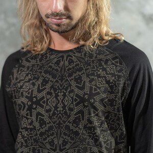 May include: A black long-sleeved shirt with a geometric pattern in a lighter shade of gray. The shirt has a raglan sleeve design.
