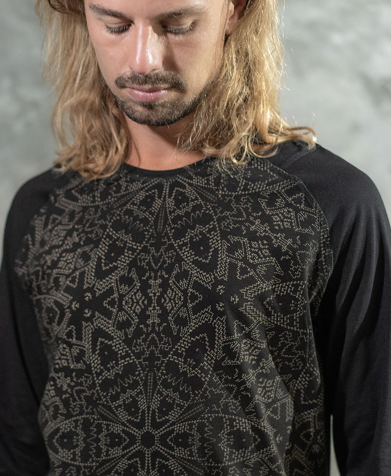 May include: A black long-sleeved shirt with a geometric pattern in a lighter shade of gray. The shirt has a raglan sleeve design.