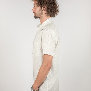 May include: A white short-sleeved button-down shirt with a small, all-over print of green leaves. The shirt has a classic fit and a pointed collar.