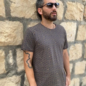 Puede incluir: Una camiseta marr&oacute;n oscuro con un peque&ntilde;o patr&oacute;n marr&oacute;n claro. La camiseta tiene cuello redondo y mangas cortas.
