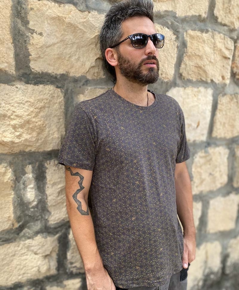 Puede incluir: Una camiseta marr&oacute;n oscuro con un peque&ntilde;o patr&oacute;n marr&oacute;n claro. La camiseta tiene cuello redondo y mangas cortas.