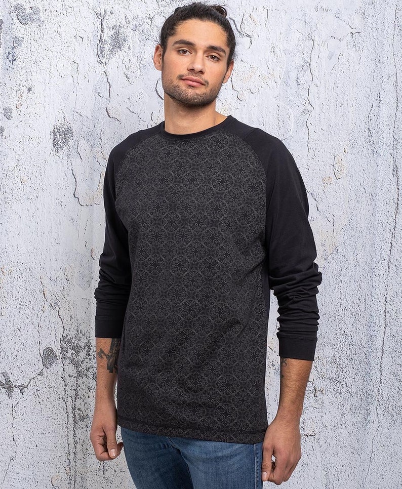 May include: A black long-sleeved shirt with a patterned design on the front and solid black sleeves. The shirt has a raglan style with a round neckline.
