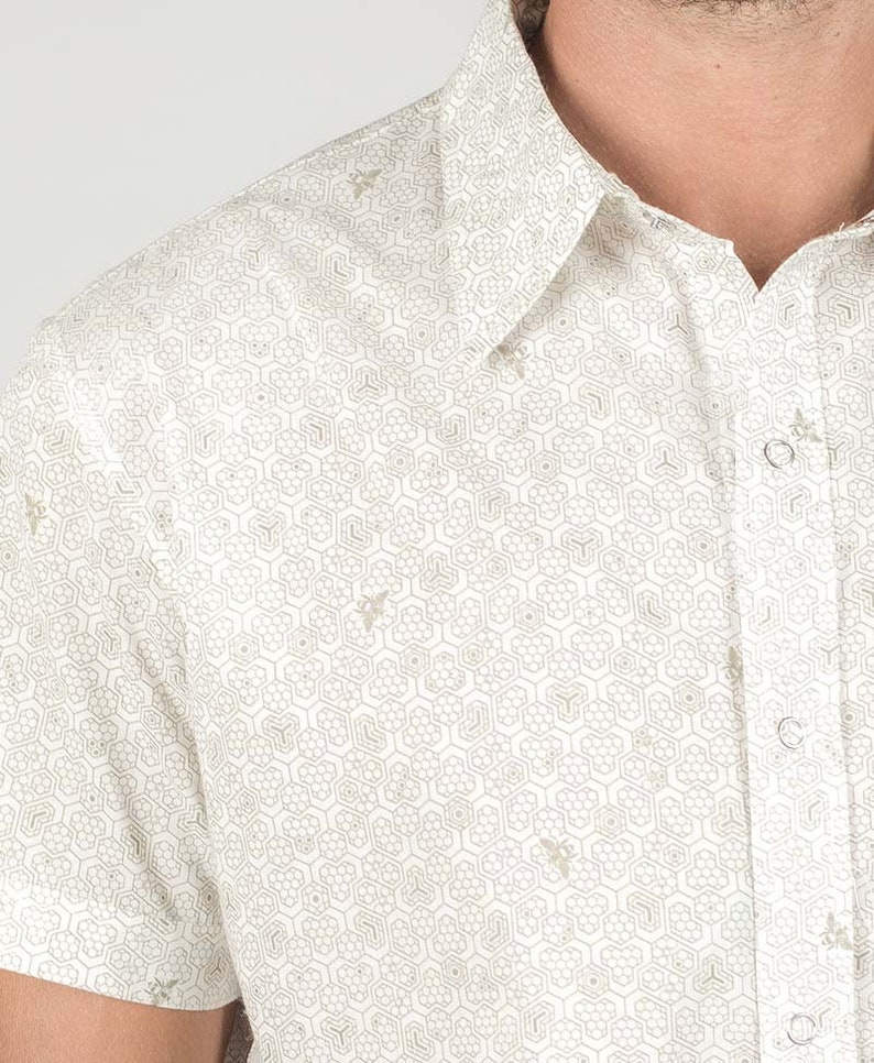 May include: White short-sleeved button-down shirt with a geometric pattern of hexagons and bees.