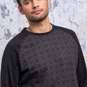 May include: Black long-sleeve shirt with a geometric pattern on the sleeves. The shirt has a crew neck and a relaxed fit.