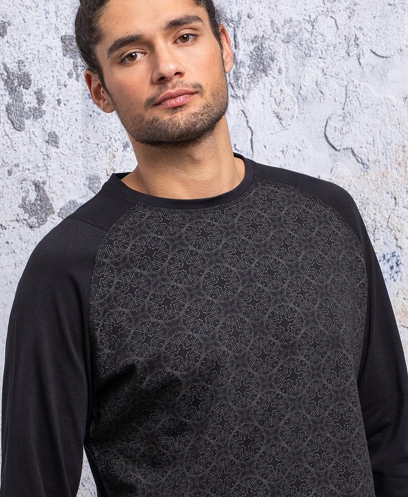 May include: Black long-sleeve shirt with a geometric pattern on the sleeves. The shirt has a crew neck and a relaxed fit.