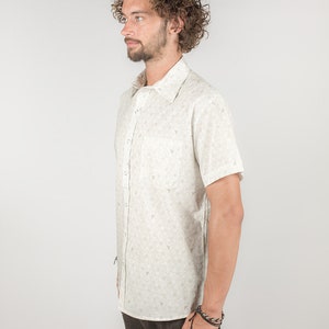 May include: A white short-sleeved button-down shirt with a small, repeating pattern of brown triangles. The shirt has a collar and a button closure.