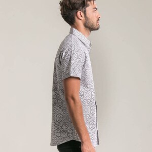 May include: A white short-sleeved button-down shirt with a black and white geometric pattern.