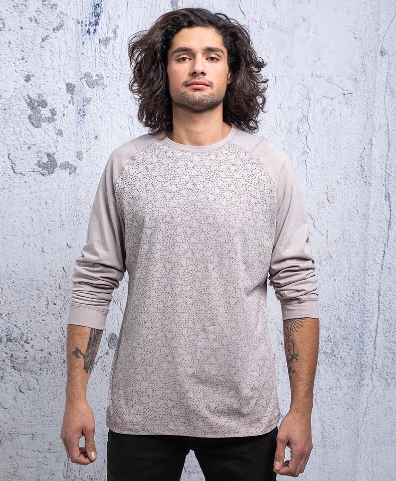 May include: A long-sleeved shirt with a geometric pattern in a light gray color. The shirt has a raglan sleeve design.